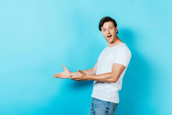 Hombre excitado en camiseta blanca apuntando con las manos sobre fondo azul - foto de stock