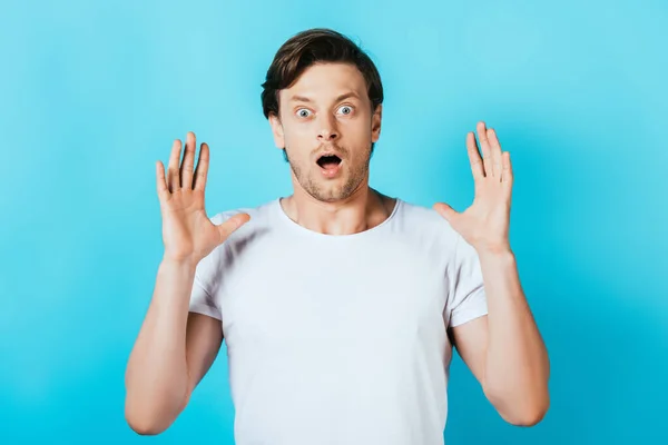 Überraschter Mann im weißen T-Shirt blickt in die Kamera auf blauem Hintergrund — Stockfoto