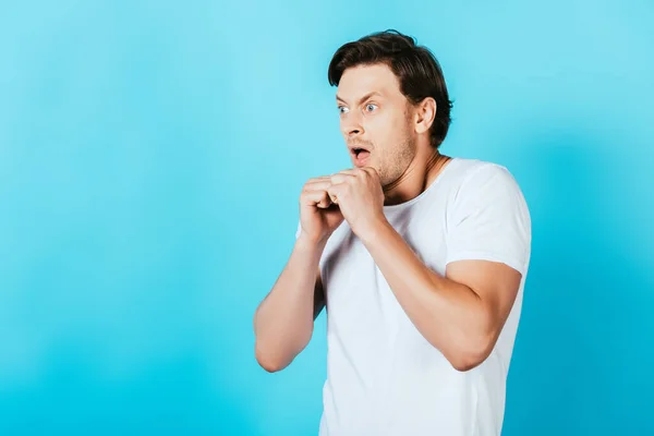 Homem louco em camiseta branca com as mãos nos punhos olhando para o fundo azul — Fotografia de Stock