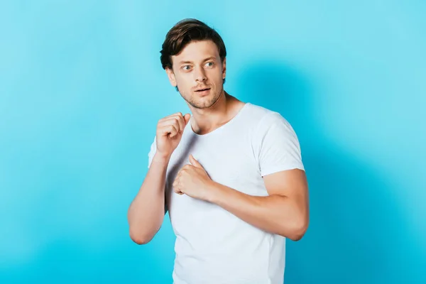 Молодой человек в белой футболке смотрит в сторону на голубом фоне — стоковое фото