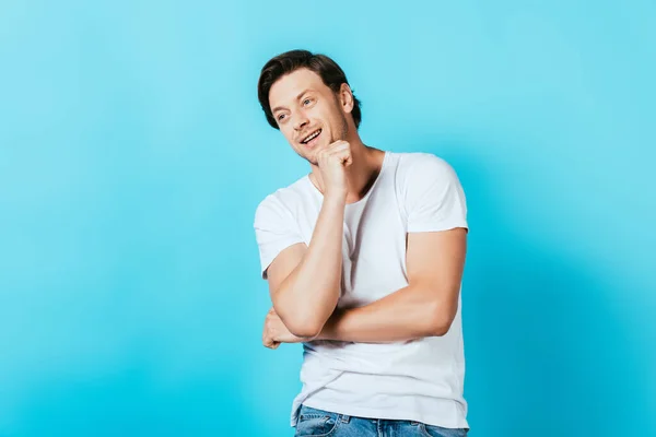 Young man with fist near chin looking away on blue background — Stock Photo