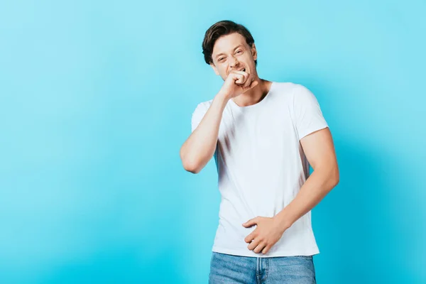 Lachender Mann mit händennahem Mund, der in die Kamera auf blauem Hintergrund blickt — Stockfoto