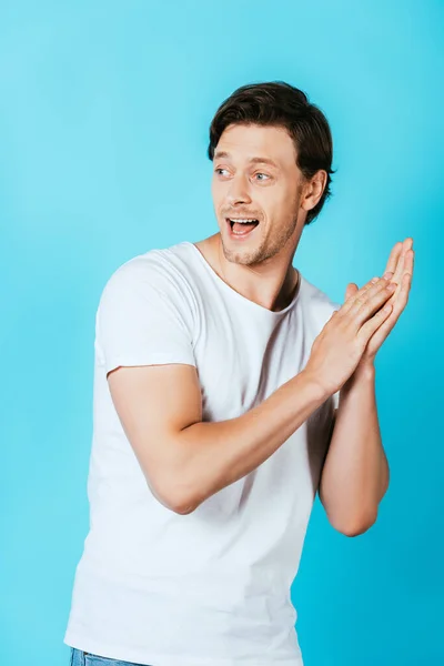 Aufgeregter Mann in weißem T-Shirt blickt vor blauem Hintergrund weg — Stockfoto