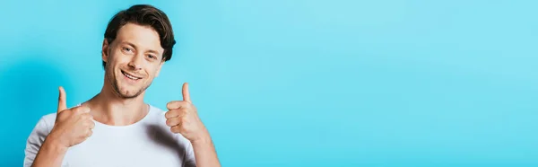 Panoramic crop of man showing thumbs up at camera on blue background — Stock Photo