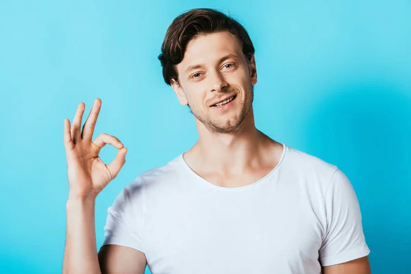 Homem de t-shirt branca mostrando gesto ok no fundo azul — Fotografia de Stock