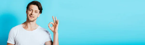 Horizontal image of young man showing ok gesture at camera on blue background — Stock Photo