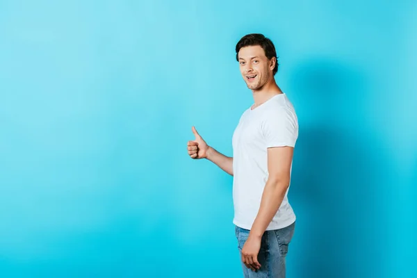 Vista lateral del hombre en camiseta blanca mostrando el pulgar hacia arriba sobre fondo azul - foto de stock
