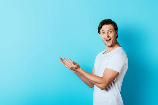 Junger Mann im weißen T-Shirt zeigt mit den Händen auf blauem Hintergrund — Stockfoto