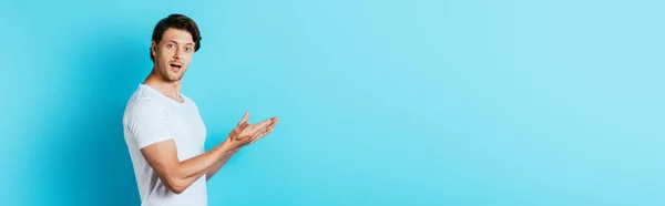 Panoramic shot of excited young man pointing with hands on blue background — Stock Photo