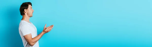 Панорамна орієнтація збудженого чоловіка, який дивиться в сторону і вказує руками на синій фон — стокове фото