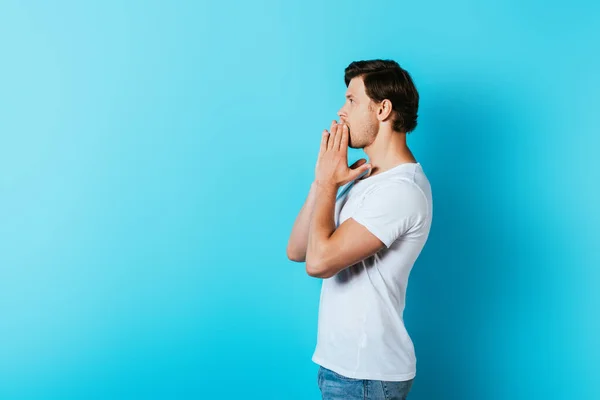 Side view of shocked man covering mouth with hands on blue background — Stock Photo