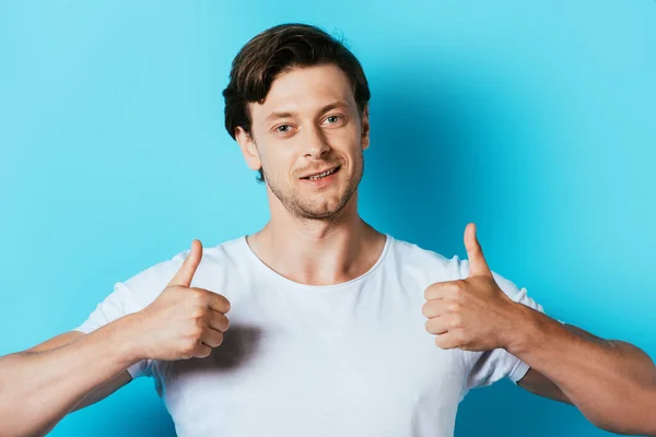 Mann im weißen T-Shirt zeigt Daumen nach oben auf blauem Hintergrund — Stockfoto