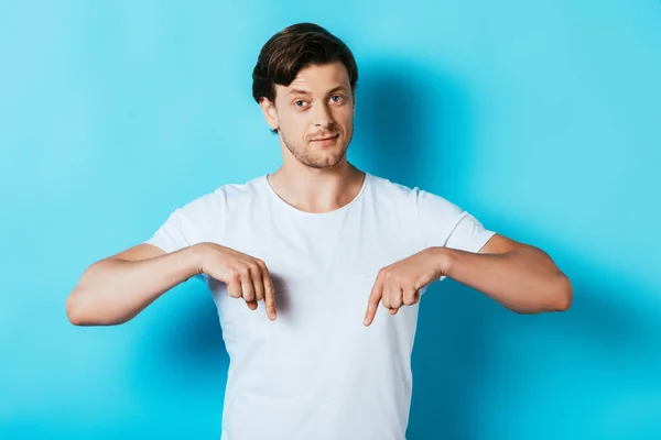 Hombre seguro en camiseta blanca señalando con los dedos sobre fondo azul - foto de stock