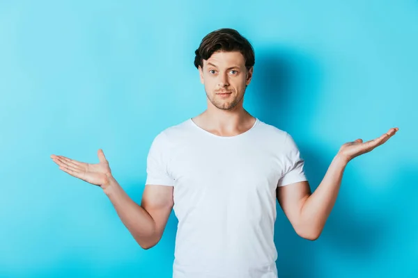 Homem confuso em t-shirt branca apontando com as mãos no fundo azul — Fotografia de Stock