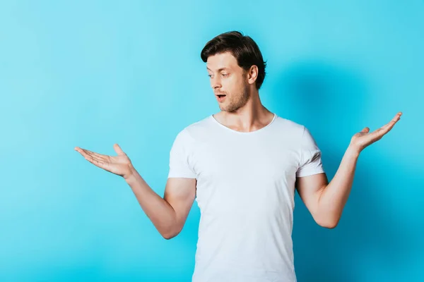 Homme excité en t-shirt blanc regardant loin tout en pointant avec les mains sur fond bleu — Photo de stock