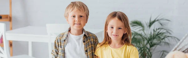 Plano panorámico de hermano y hermana mirando a la cámara mientras está de pie en casa - foto de stock