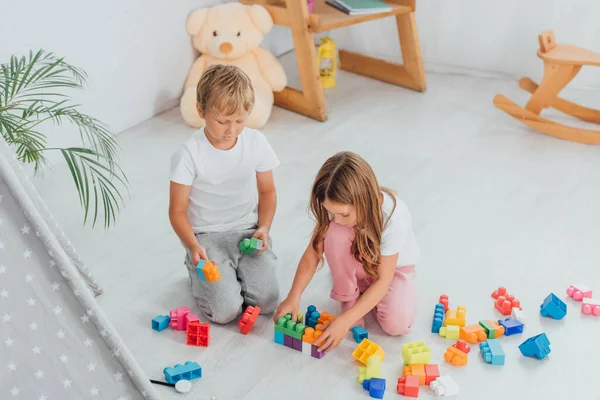High angle view of children playing with building blocks while sitting on floor in pajamas — Stock Photo