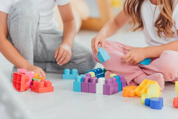 Vista recortada de niños jugando con bloques de construcción mientras están sentados en el piso en pijama - foto de stock