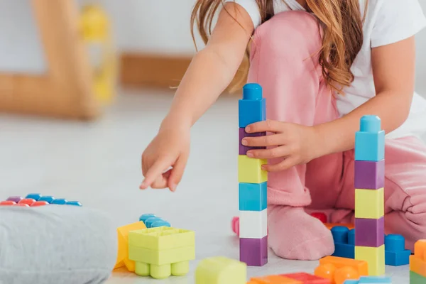 Обрізаний вид дитини, який вказує пальцем під час гри з барвистими будівельними блоками на підлозі — стокове фото