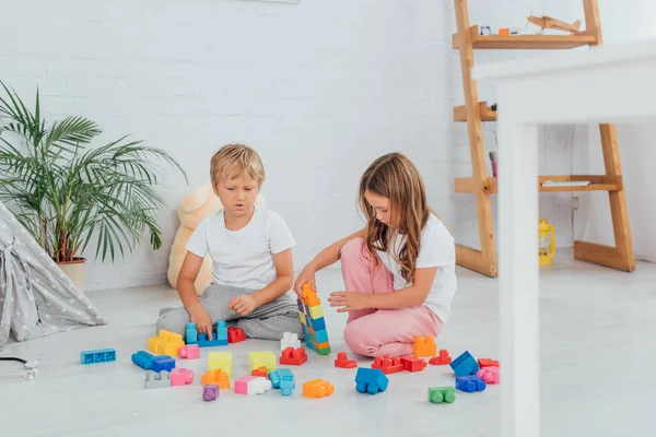 Селективное внимание детей в пижамах, сидящих на полу и играющих со строительными блоками — стоковое фото