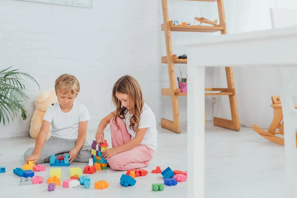 Messa a fuoco selettiva del fratello e della sorella concentrati in pigiama seduti sul pavimento e che giocano con i mattoni — Foto stock