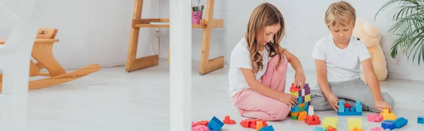 Горизонтальная концепция сестры и брата в пижаме, сидящих на полу и играющих со строительными блоками — стоковое фото