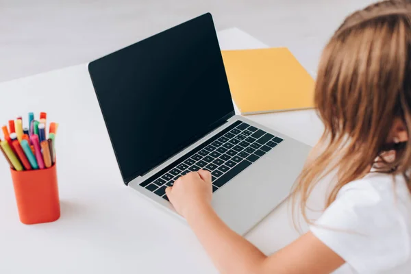 Vista de ángulo alto de la niña utilizando el ordenador portátil con pantalla en blanco cerca de titular de la pluma y portátil - foto de stock