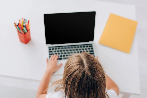 Overhead view of girl using laptop with blank screen near pen holder and notebook — Stock Photo