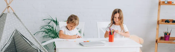 Imagem horizontal de irmão e irmã em pijama desenho com canetas de feltro na mesa perto de crianças wigwam — Fotografia de Stock