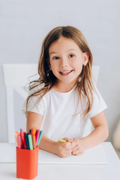 Foyer sélectif de fille excitée en t-shirt blanc tenant feutre stylo et en regardant la caméra — Photo de stock