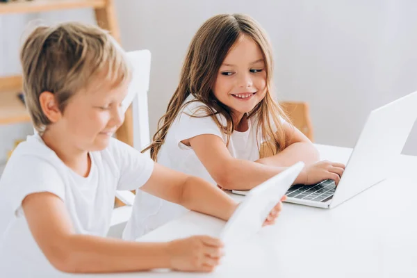 Selektiver Fokus des Mädchens, das seinen Bruder ansieht, während es am Tisch sitzt und gemeinsam Laptops benutzt — Stockfoto