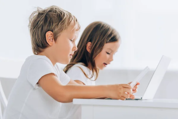 Enfoque selectivo de niño y niña concentrados usando computadoras portátiles en casa - foto de stock