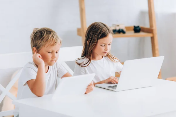 Concentrated brother and sister sitting at while table and using laptops together — Stock Photo