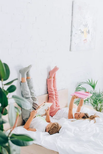 Selective focus of brother and sister in pajamas lying with legs on wall and reading books — Stock Photo