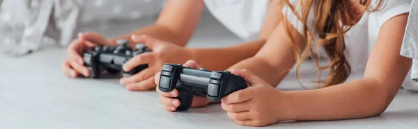 KYIV, UKRAINE - JULY 21, 2020: cropped view of brother and sister lying on floor and playing video game with joysticks, horizontal image — Stock Photo