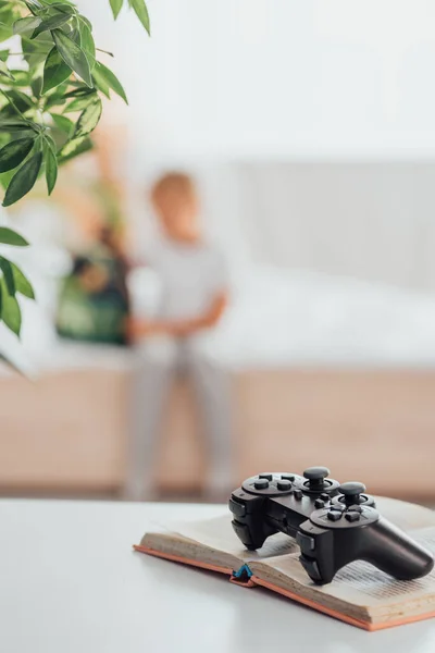 KYIV, UCRAINA - 21 LUGLIO 2020: focus selettivo del joystick su libro aperto e ragazzo seduto sul letto vicino allo zaino della scuola sullo sfondo — Foto stock