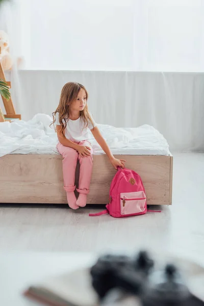 Selektiver Fokus eines Mädchens im Schlafanzug, das im Schlafanzug auf dem Boden sitzend den Schulrucksack berührt — Stockfoto