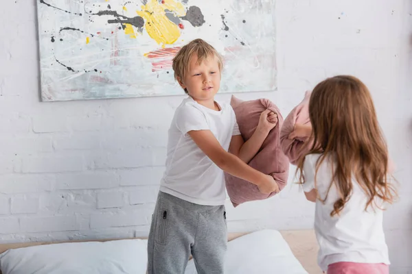 Siblings in pajamas having fun while fighting with pillow in bedrooms — Stock Photo