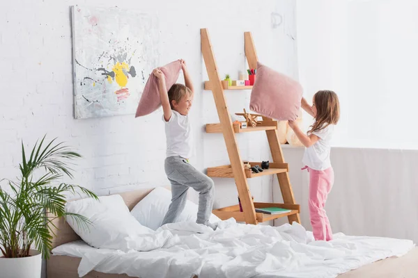 Frère et soeur en pyjama s'amuser tout en se battant avec des oreillers dans la chambre — Photo de stock