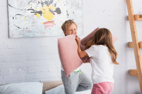 Excited boy and girl in pajamas fighting with pillows while having fun in bedroom — Stock Photo