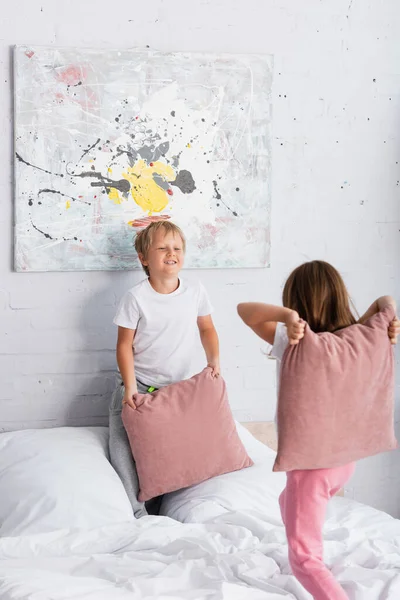 Брат и сестра в пижаме веселятся, дерясь с подушками в спальнях — стоковое фото