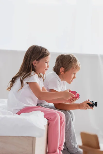 KYIV, UCRANIA - 21 de julio de 2020: vista lateral de niños enfocados en pijamas jugando videojuegos - foto de stock
