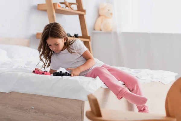 KYIV, UKRAINE - JULY 21, 2020: chid in pajamas sitting on bed and looking at joysticks — Stock Photo