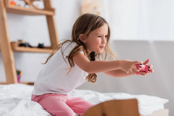 KYIV, UKRAINE - JULY 21, 2020: concentrated girl in pajamas playing video game with joystick while sitting on bed — Stock Photo