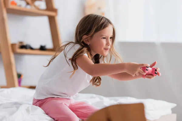 KYIV, UKRAINE - 21 JUILLET 2020 : fille concentrée en pyjama jouant à un jeu vidéo avec un joystick assis sur le lit — Photo de stock