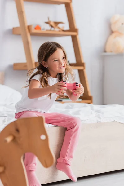 KYIV, UKRAINE - JULY 21, 2020: selective focus of girl in pajamas sitting on bed and playing video game — Stock Photo