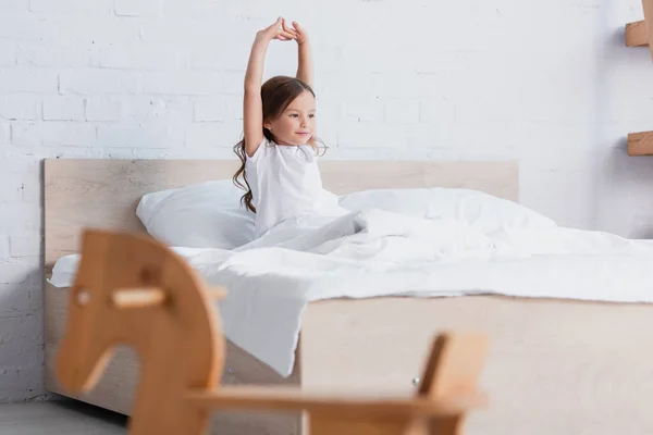 Selective focus of awakened kid stretching while sitting in bed — Stock Photo