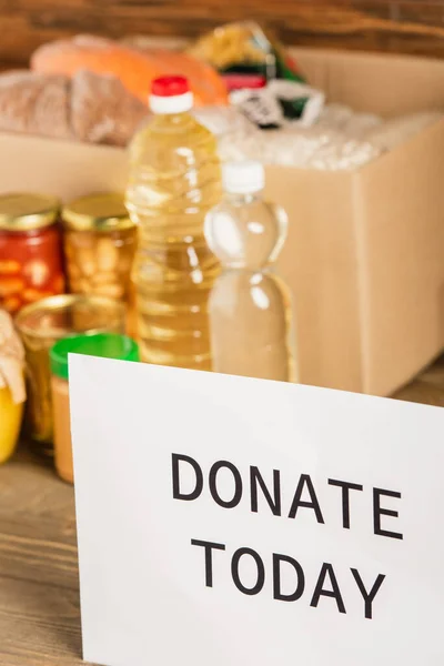 Selektiver Fokus von Karton mit Lebensmitteln und Spendenkarte heute auf Holzgrund, Charity-Konzept — Stockfoto