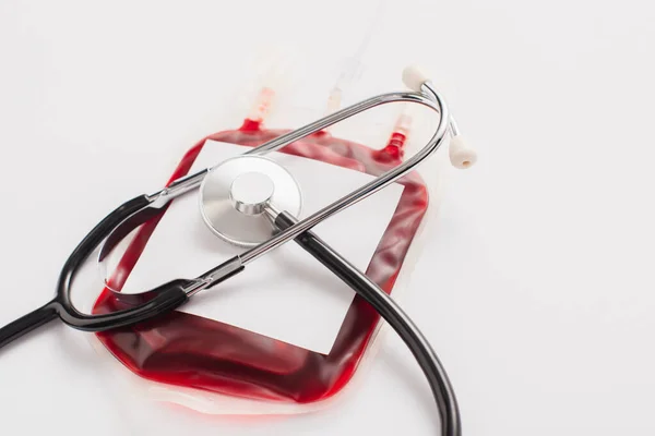 Confezione di donazione di sangue con etichetta bianca e stetoscopio su bianco — Foto stock