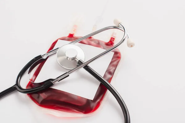 Blood donation package with blank label and stethoscope on white — Stock Photo